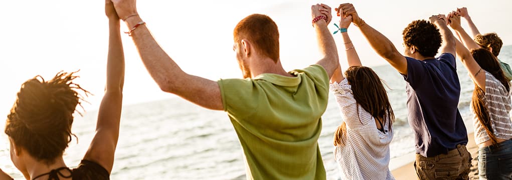 People holding hands above their heads in worship while standing on a beach