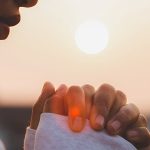 Woman praying in front of a sunrise (or sunset)