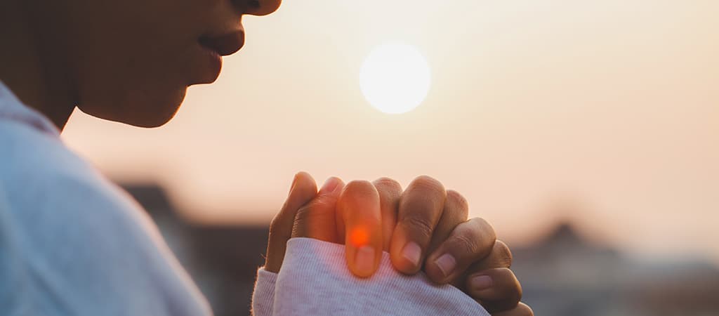 Woman praying in front of a sunrise (or sunset)